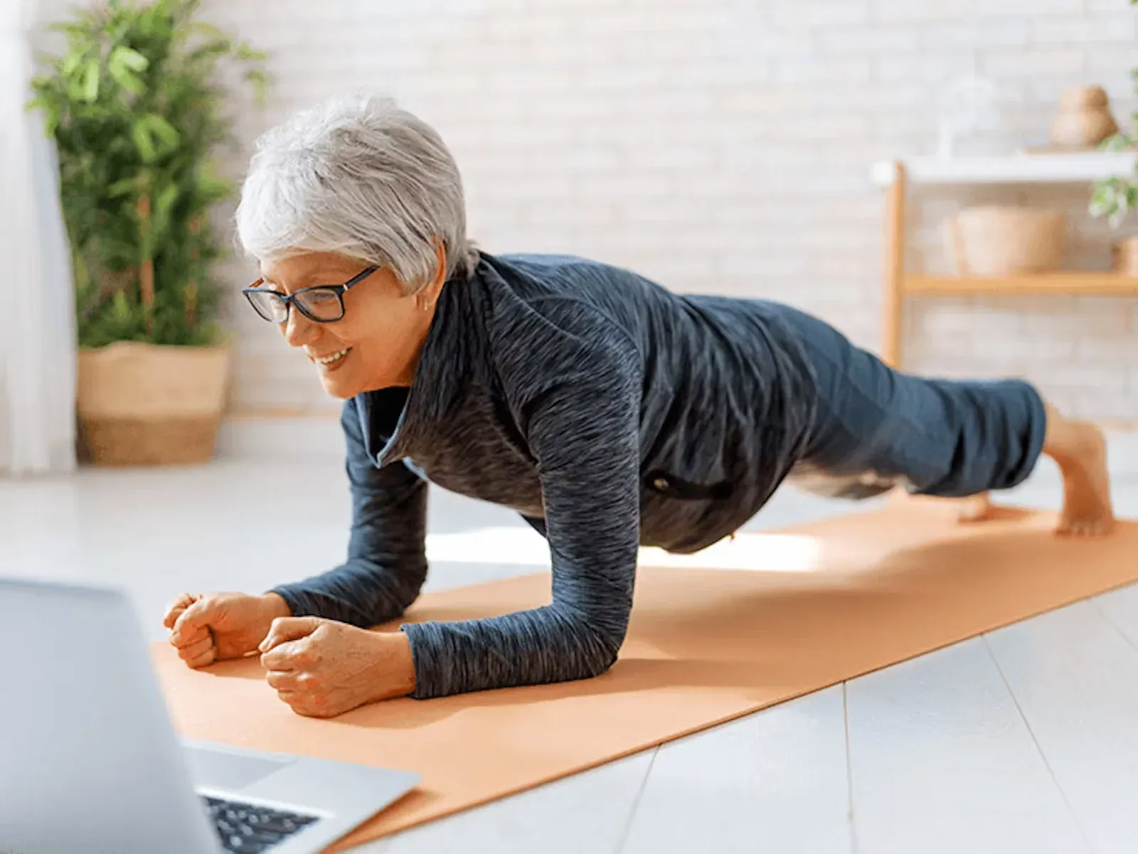 A woman sitting on a mat at home, following a live session on a propped-up tablet