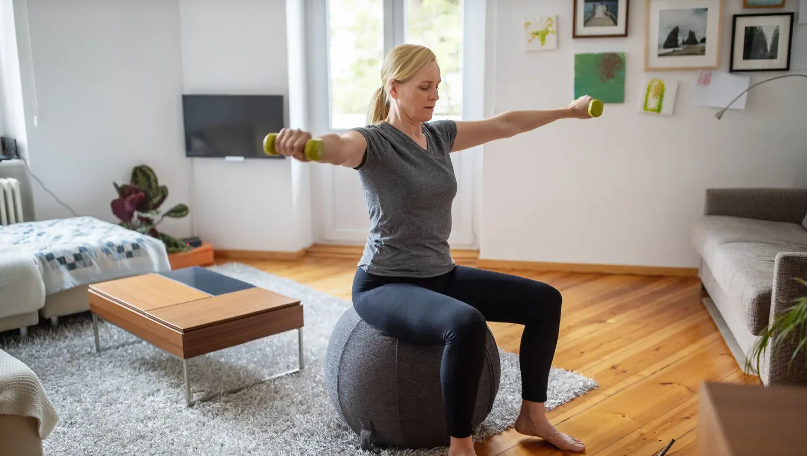 A woman training with light dumbbells while seated on a stability ball at home