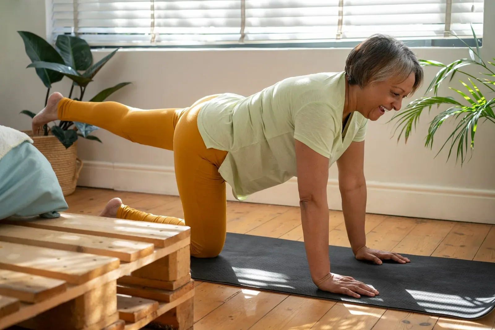 A woman on a mat at home in a hands-and-knees position with one leg extended behind her