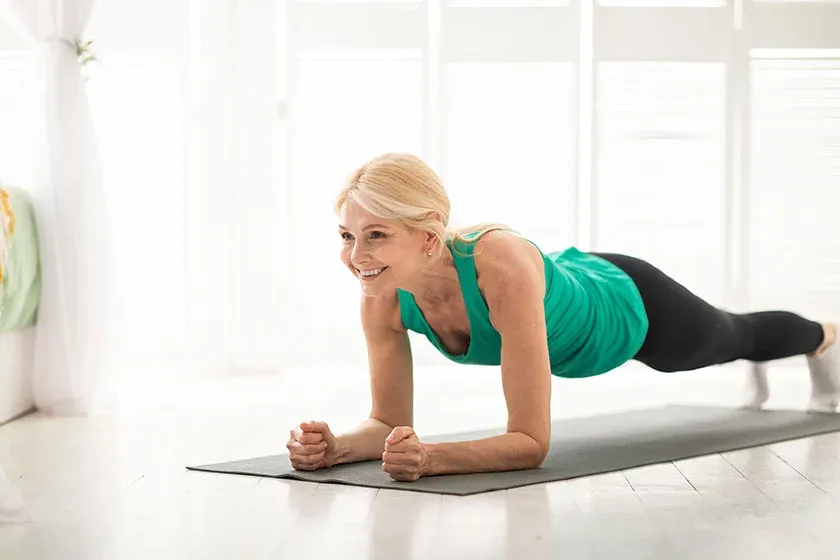 A woman holding a forearm plank on a mat at home in bright daylight